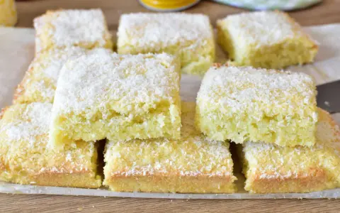 Fette di torta al cocco, soffici e dorate, cosparse di scaglie bianche. Un dolce profumato e invitante.