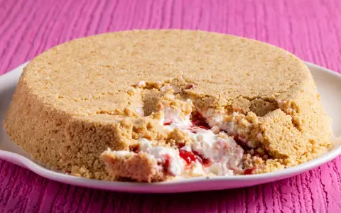Cheesecake con yogurt greco e marmellata di fragole, con una crosta friabile di biscotti. Un morso goloso rivela il ripieno cremoso.