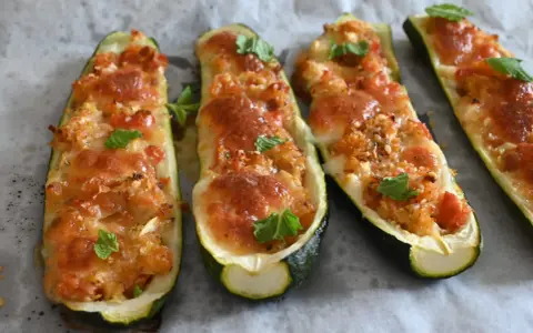 Zucchine tonde ripiene al forno, dorate e filanti, guarnite con foglie di menta fresca.