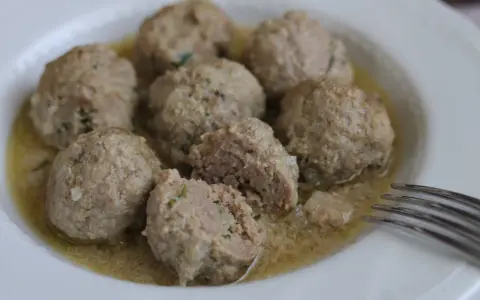 Polpette in umido, morbide e succulente, servite in un piatto bianco con un sughetto invitante.