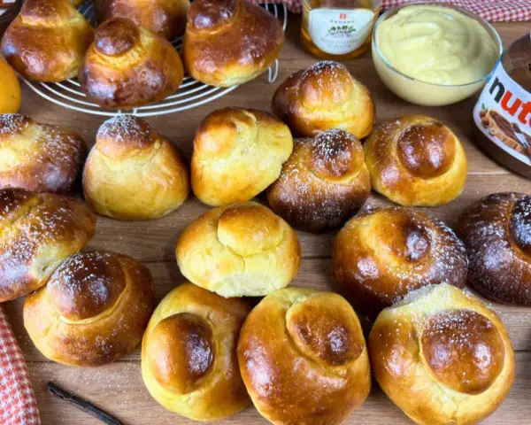 Tanti brioche col tuppo dorati, alcuni spolverati di zucchero a velo, pronti per essere farciti con crema o Nutella.