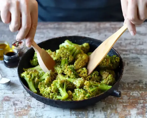 Broccoli in padella, condito con olio e spezie, viene mescolato con due palette di legno.