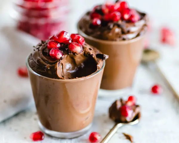 Due bicchierini di golosa mousse al cioccolato, guarniti con chicchi di melagrana e scaglie di cioccolato.
