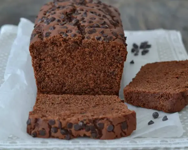 Un soffice plumcake al cioccolato, ricco di gocce, è tagliato a fette su carta da forno.