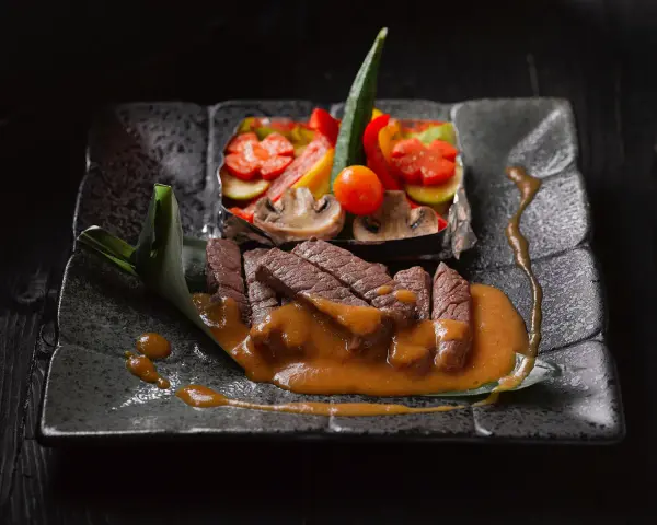 Straccetti di manzo succulenti su un piatto scuro, accompagnati da verdure miste e una salsa cremosa.