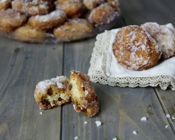 Frittelle di riso ricetta della nonna: dolcetti dorati e zuccherati, uno aperto rivela l'interno soffice e i chicchi d'uva passa.