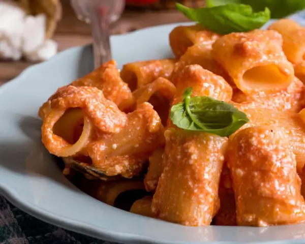 Piatto di pasta ricotta e pomodorini, condita con una cremosa salsa e guarnita con foglie di basilico fresco.