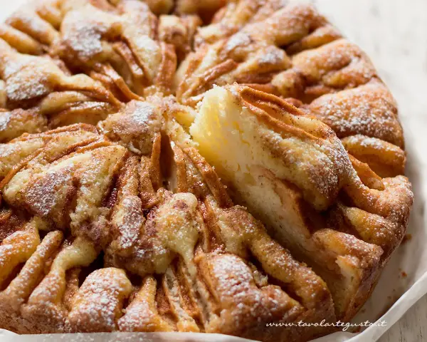 Una deliziosa torta di mele, cosparsa di zucchero a velo, con una fetta sollevata che rivela la morbida consistenza.
