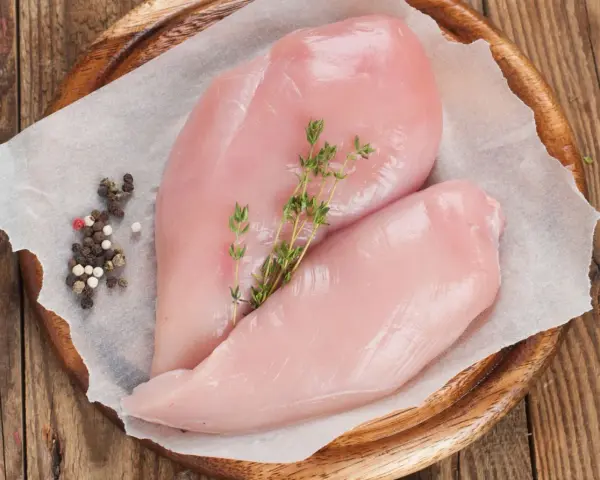 Due petti di pollo crudi, freschi e succulenti, adagiati su carta forno con pepe misto e rametti di timo.