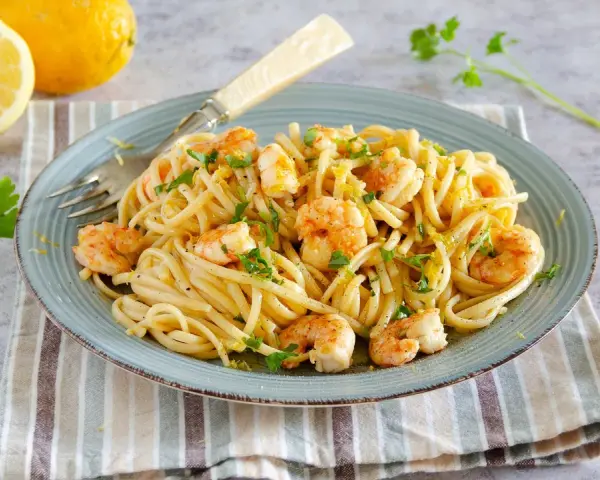Un piatto di pasta con gamberetti, condita con limone e prezzemolo, accompagnata da limoni freschi e parmigiano.
