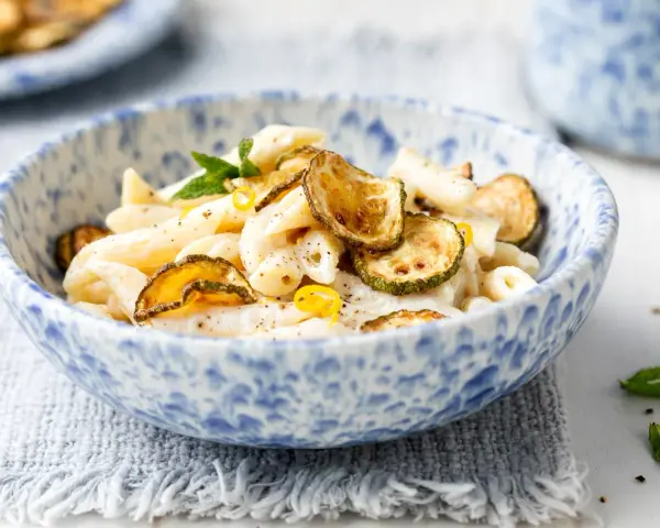 Piatto di pasta cremosa con ricotta e zucchine croccanti, guarnito con scorza di limone e menta.