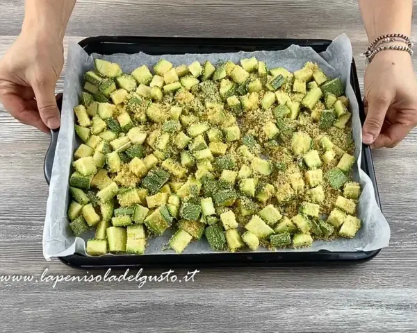 Zucchine gratinate al forno pronte per essere infornate, tagliate a cubetti e cosparse di pangrattato.