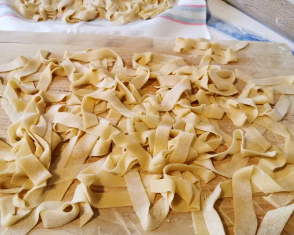 Fettuccine fresche, tagliatelle fatte in casa sparse su un tagliere di legno, pronte per essere cucinate.