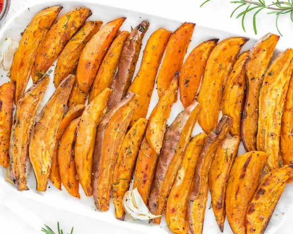 Patate dolci al forno, tagliate a spicchi e condite con erbe aromatiche, servite su un piatto bianco.