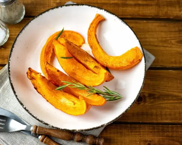 Fette di zucca al forno dorate e profumate, guarnite con rosmarino fresco, pronte per essere gustate.