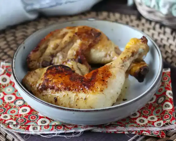 Cosce di pollo in padella, dorate e succulente, servite in una ciotola su un tovagliolo decorato.