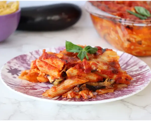 Piatto di pasta alla siciliana con melanzane, pomodoro e basilico, appena sfornata.