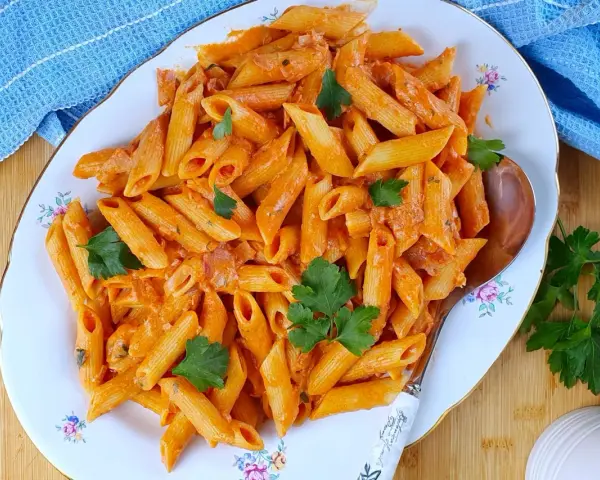Piatto di penne al baffo cremose, guarnite con prezzemolo fresco, pronte per essere gustate.