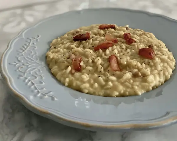Un cremoso risotto con ceci e pancetta croccante, servito su un piatto azzurro decorato.