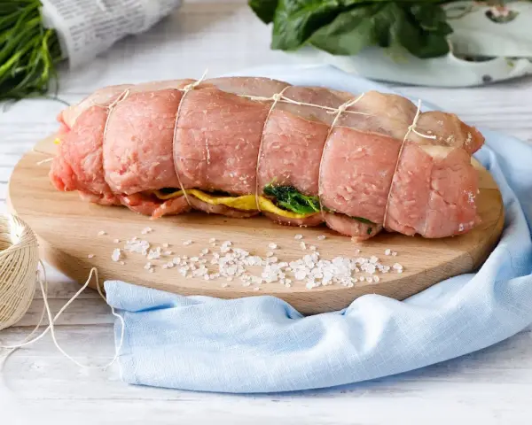Un arrosto al forno pronto per essere cucinato, legato con spago, su un tagliere con sale grosso e verdure.