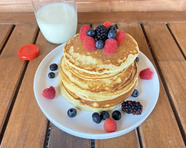 Pila di pancake senza zucchero guarnita con frutti di bosco freschi, accompagnata da un bicchiere di latte.
