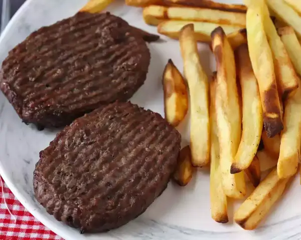 Due hamburger in friggitrice ad aria con patatine fritte dorate su un piatto bianco.