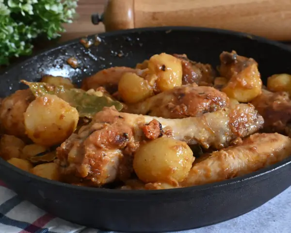 Un saporito pollo in umido con patate e alloro, cotto in una padella di ghisa, pronto per essere gustato.
