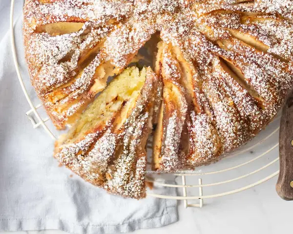 Deliziosa torta di mele in friggitrice ad aria, spolverata di zucchero a velo, con una fetta tagliata per mostrare il morbido interno.