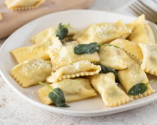 Piatto di ravioli del plin, dorati e spolverati di parmigiano, guarniti con foglie di salvia fresca.