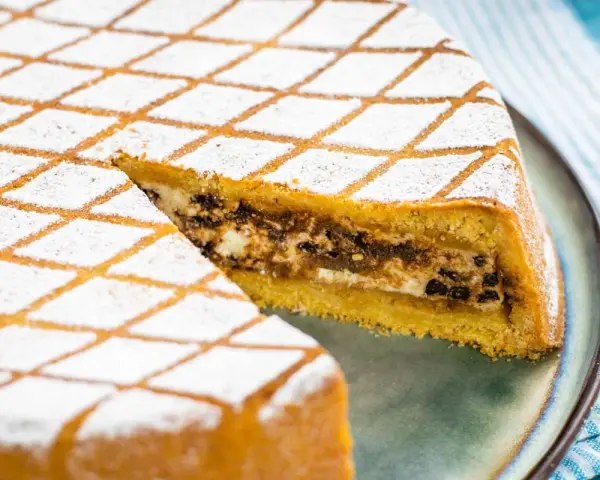 Una fetta di cassata al forno, con la sua copertura a rombi di zucchero a velo, rivela un ripieno goloso di ricotta e cioccolato.
