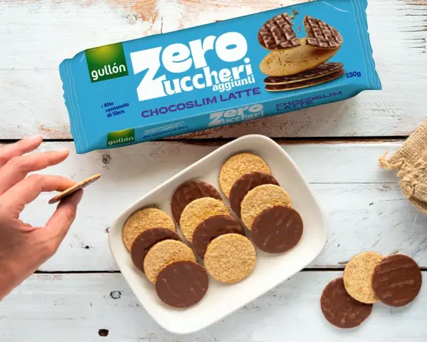 Biscotti senza zucchero Gullón Chocoslim Latte, alcuni ricoperti di cioccolato, su un piatto bianco. Una mano ne prende uno.