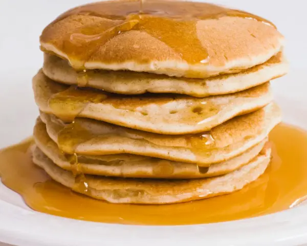 Pila di pancake dorati, inzuppati di sciroppo d'acero. Perfetti per una ricetta pancake proteici sana e golosa.