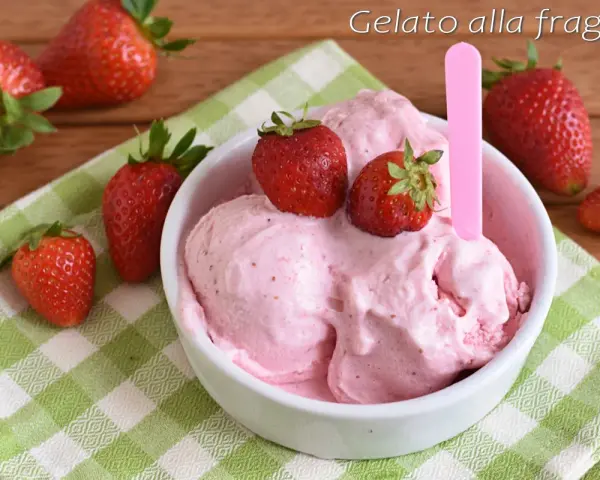 Una ciotola di cremoso gelato alla fragola, guarnito con fragole fresche, su una tovaglietta a quadri verdi.