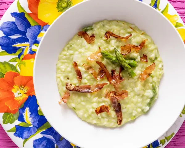 Un cremoso risotto asparagi e speck, guarnito con punte di asparagi freschi e croccanti listarelle di speck.