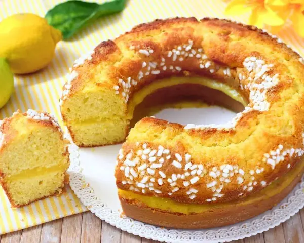 Un soffice ciambellone al limone, decorato con perline di zucchero, con una fetta tagliata che rivela un ripieno cremoso.