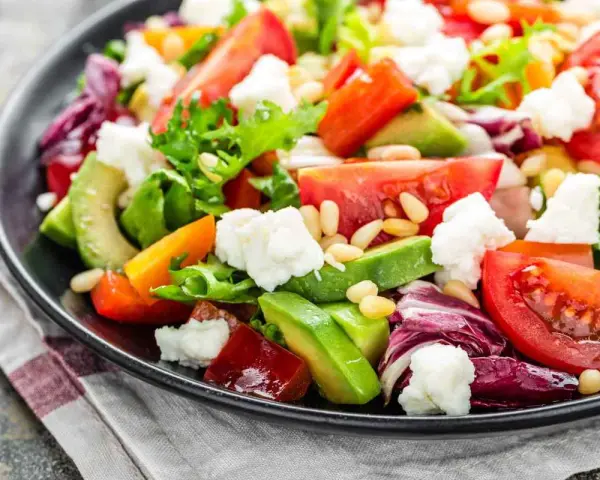 Insalata fresca con pomodori, lattuga, formaggio e avocado a fette, guarnita con pinoli.