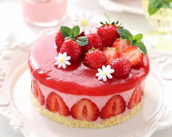 Deliziosa bavarese alle fragole, ricoperta da una gelatina rossa brillante e decorata con fragole fresche, menta e fiorellini bianchi.