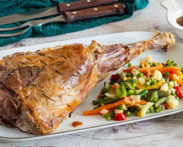 Succulento agnello al forno, dorato e profumato, servito con un contorno di verdure miste colorate.