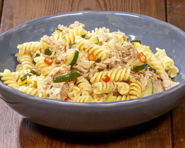 Fusilli con zucchine, tonno e peperoncino in una ciotola blu su un tavolo di legno. Un piatto semplice e gustoso.