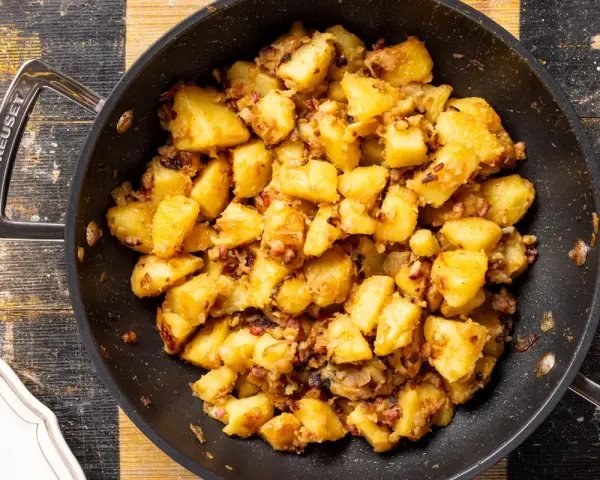 Patate in tecia dorate e croccanti, con pezzetti di pancetta e cipolla, pronte per essere gustate.