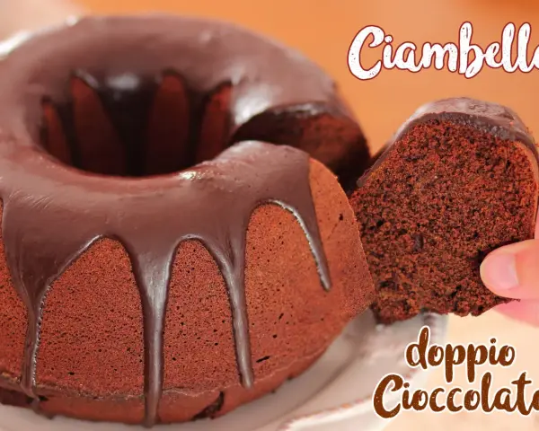 Ciambellone al cioccolato con glassa fondente che cola. Una fetta viene sollevata, mostrando la morbidezza dell'impasto.