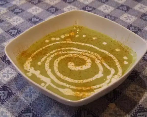 Una ciotola quadrata bianca contiene una vellutata crema di piselli, decorata con un vortice di panna e una spolverata di spezie.
