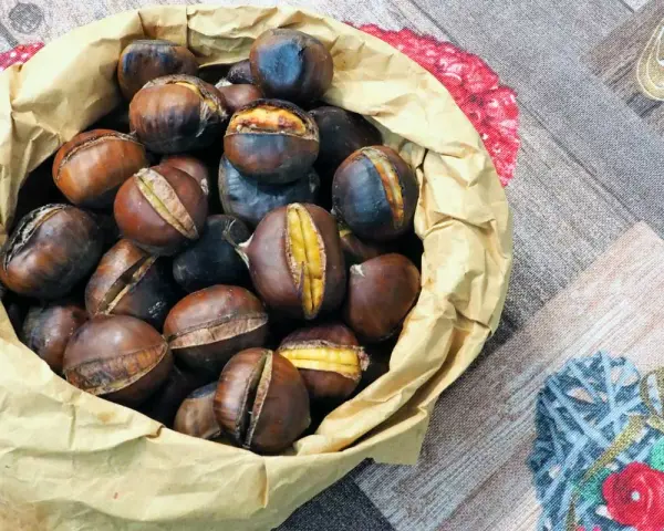 Castagne in friggitrice ad aria, pronte per essere gustate. Un sacchetto di carta marrone trabocca di castagne calde e dorate, alcune con tagli che rivelano il loro interno morbido.
