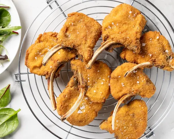 Deliziose costolette d'agnello fritte, dorate e croccanti, cosparse di sale grosso, su una griglia. Accanto, un'insalata fresca.