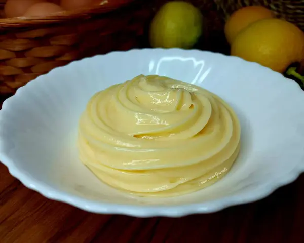 Una spirale di soffice crema al limone in una ciotola bianca, con limoni e uova sullo sfondo.
