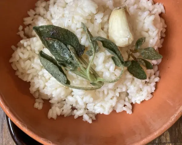 Riso in cagnone, profumato con aglio e salvia croccante, servito in una ciotola di terracotta.