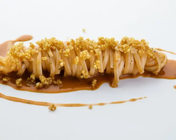 Pasta con carciofi Cannavacciuolo, un piatto elegante con pasta lunga, salsa cremosa e croccanti germogli di quinoa.