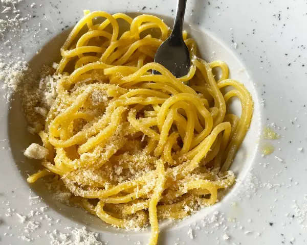 Un piatto di pasta in bianco, spaghetti conditi con formaggio grattugiato e un filo d'olio, pronti per essere gustati.