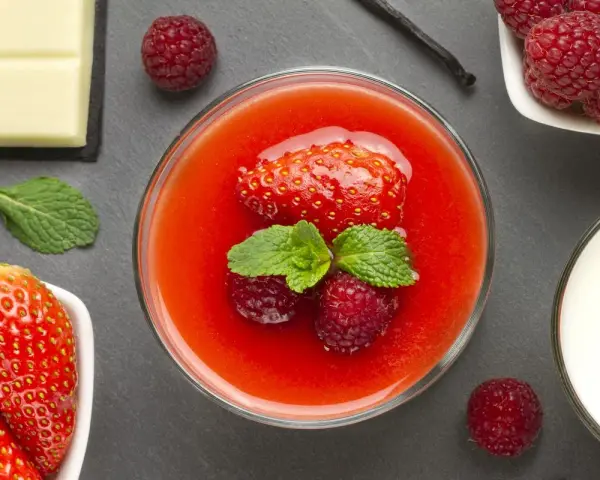 Delizioso coulis di fragole guarnito con fragola, lamponi e menta. Accanto, cioccolato bianco, lamponi freschi e un bicchiere di latte.