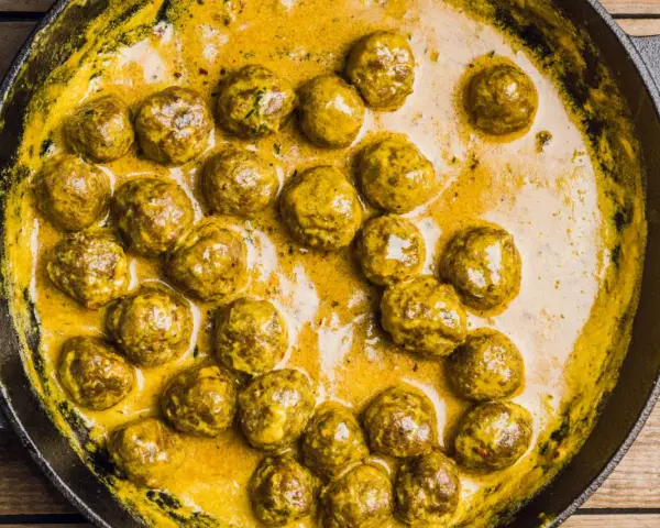 Polpette in bianco cremose in padella, dorate e succulente, immerse in una salsa gialla e invitante.